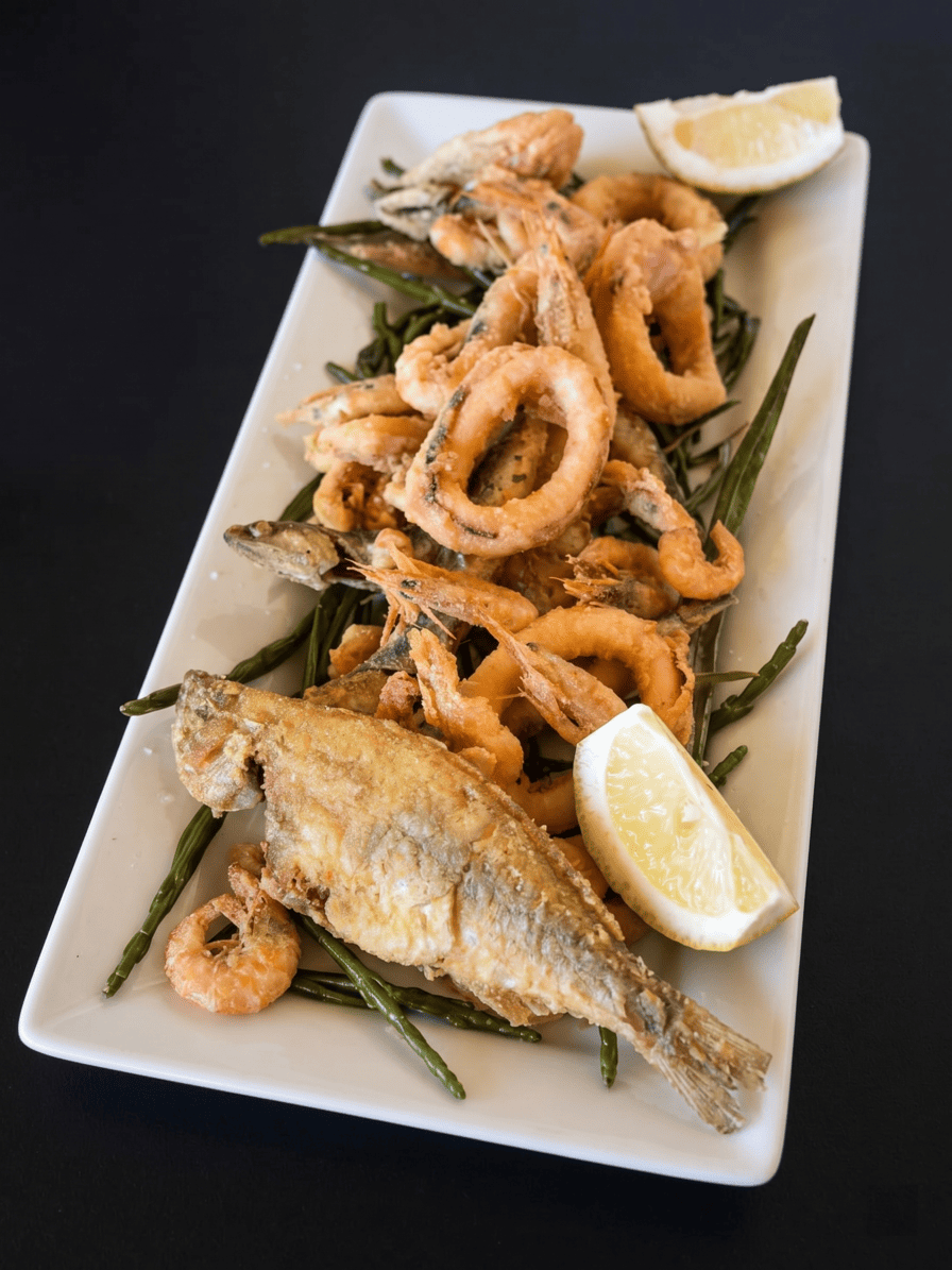 Plato de fritureta de pescado variado con calamares y rodaja de limón.