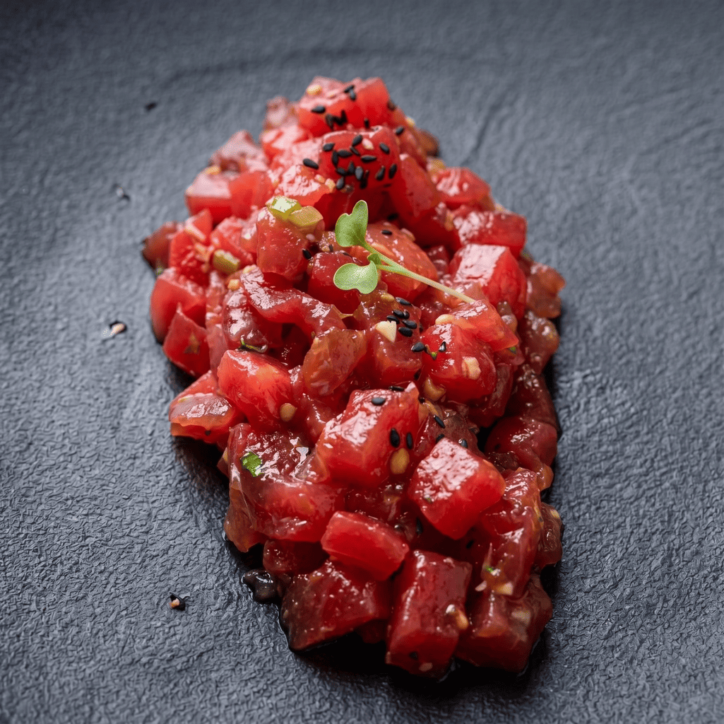 Tartar de carne roja o atún rojo aliñado sobre plato oscuro.