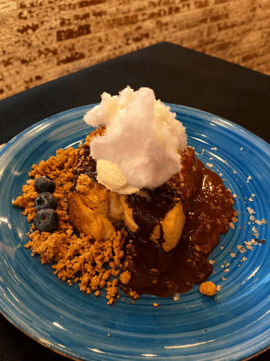 Postre gourmet en plato azul con tierra de galleta, helado, chocolate y algodón de azúcar.